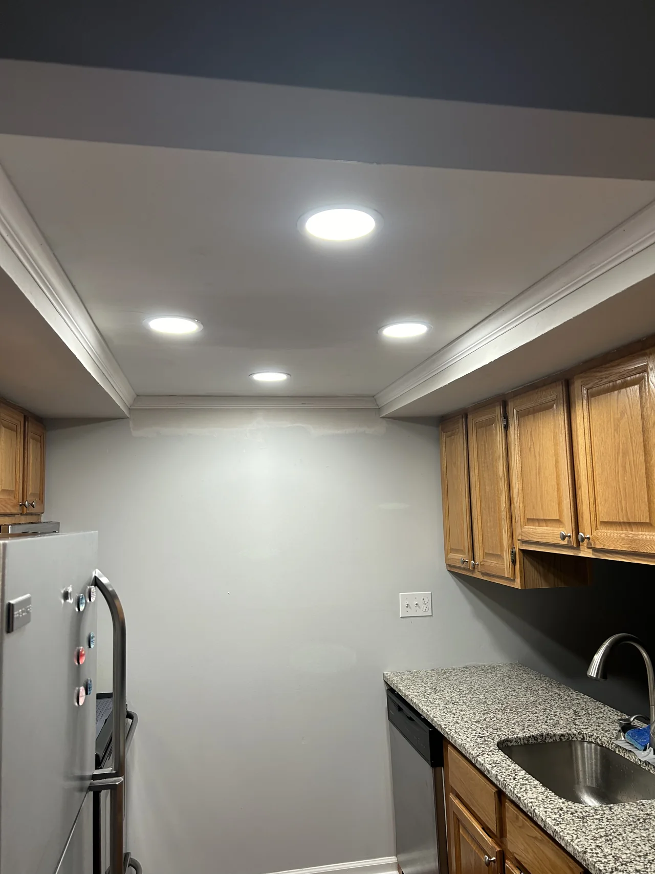 After ceiling work: recessed lights and crown molding above the same wood cabinets