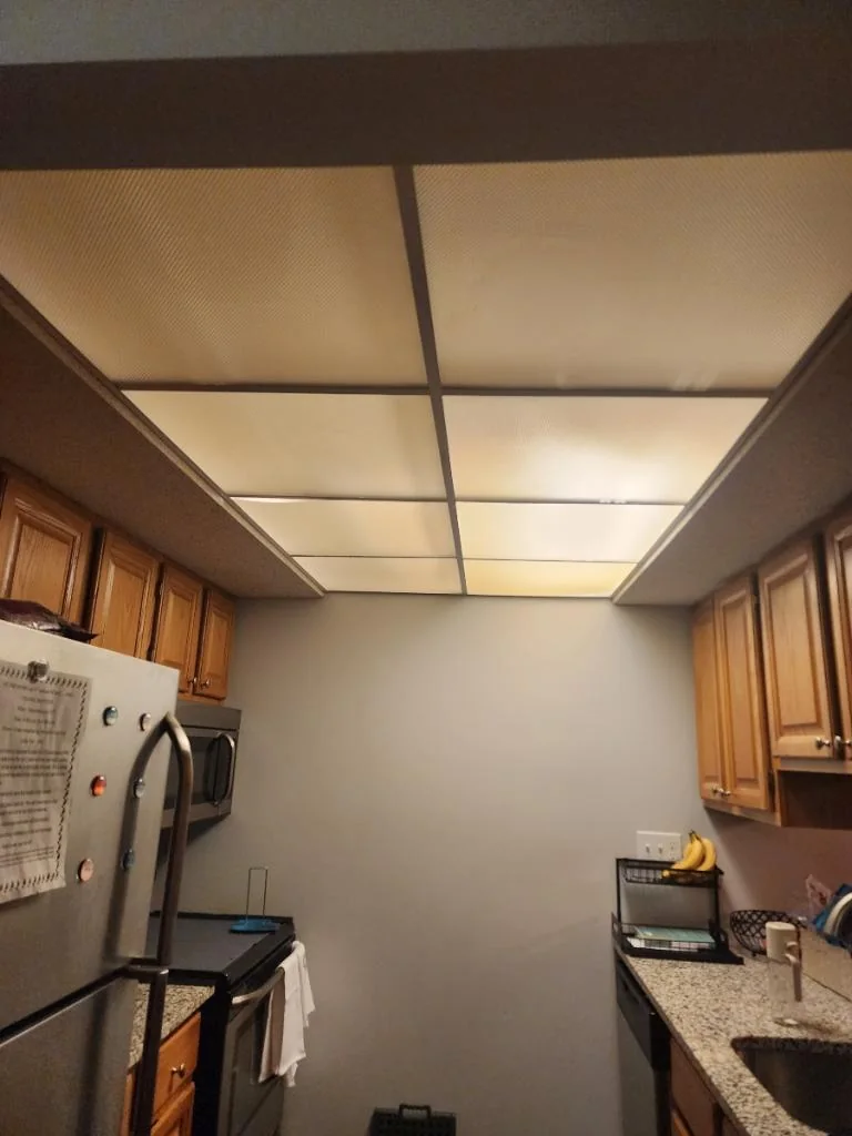 Before: kitchen with large ceiling light panels above wood cabinets